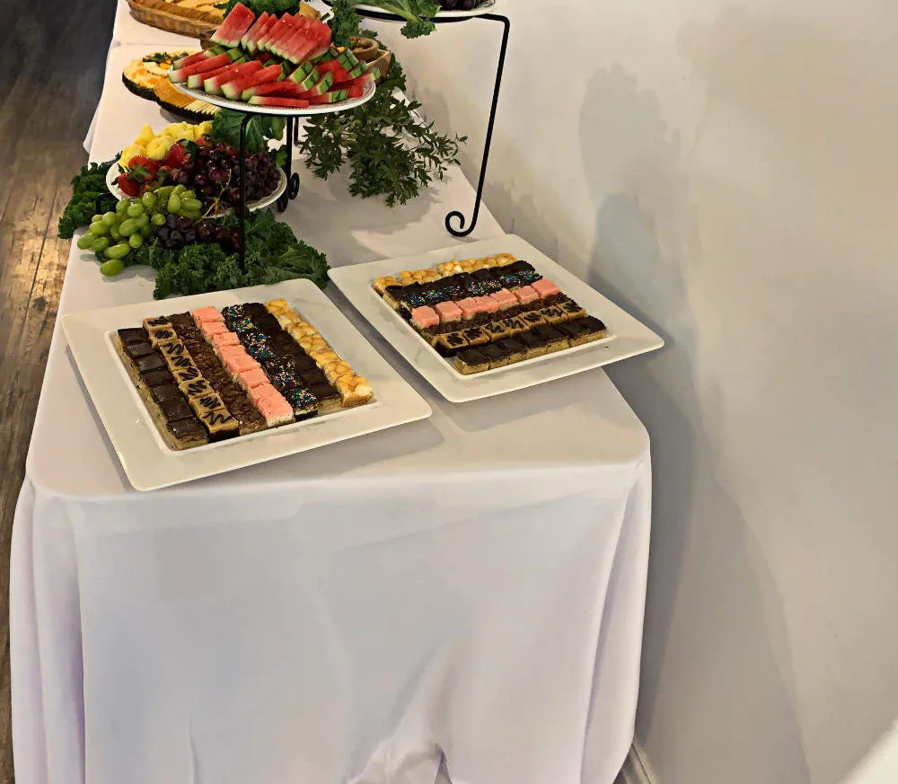 A table with a white table cloth and various desserts and fruit arranged on it.